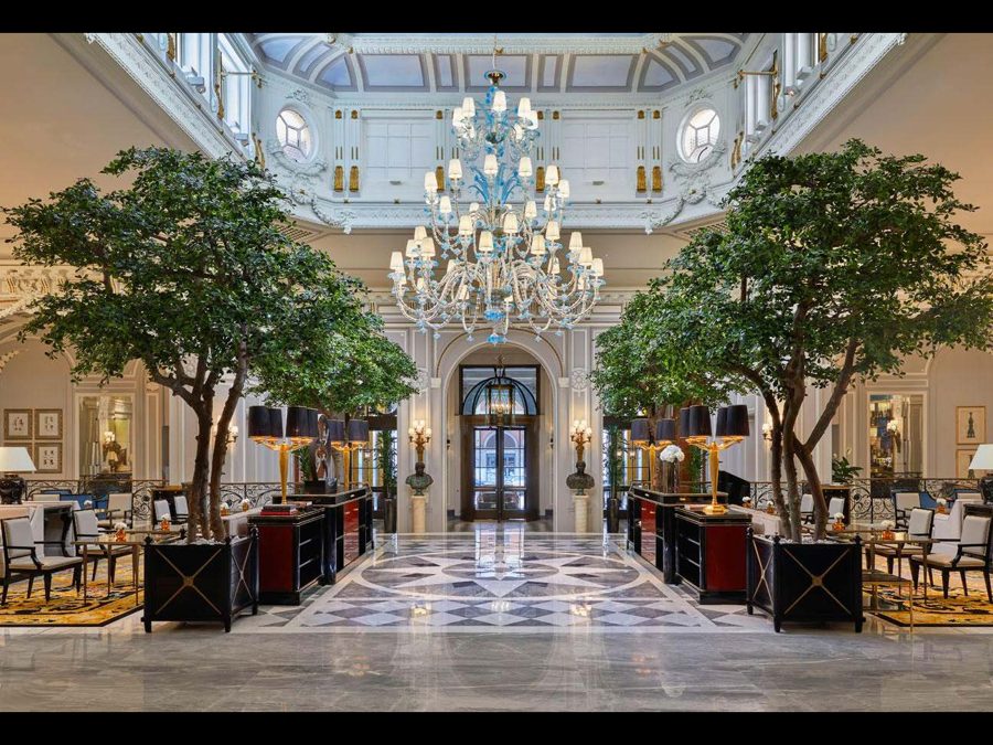 Two large artificial ficus trees in a grand hotel lobby with a chandelier