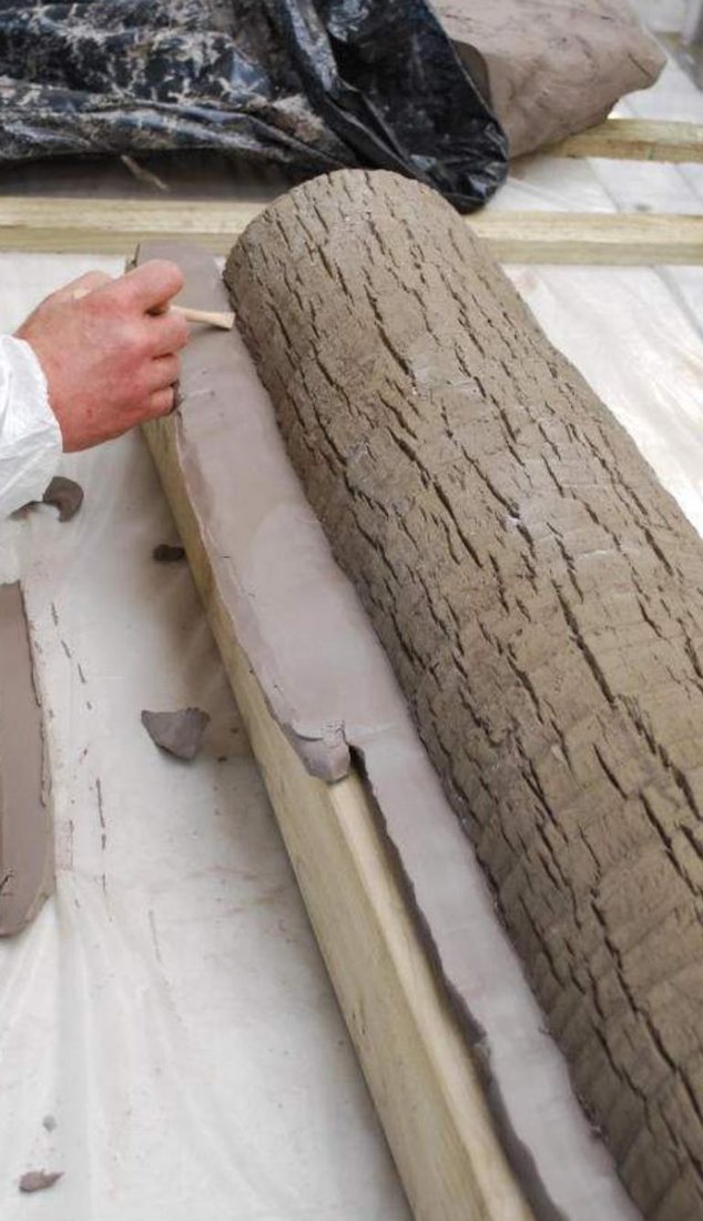 A hand pressing a freshly cast bark skin onto a trunk form