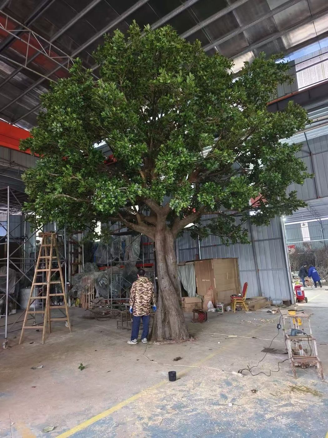 A craftsman standing beside a very large artificial tree assembled in the workshop